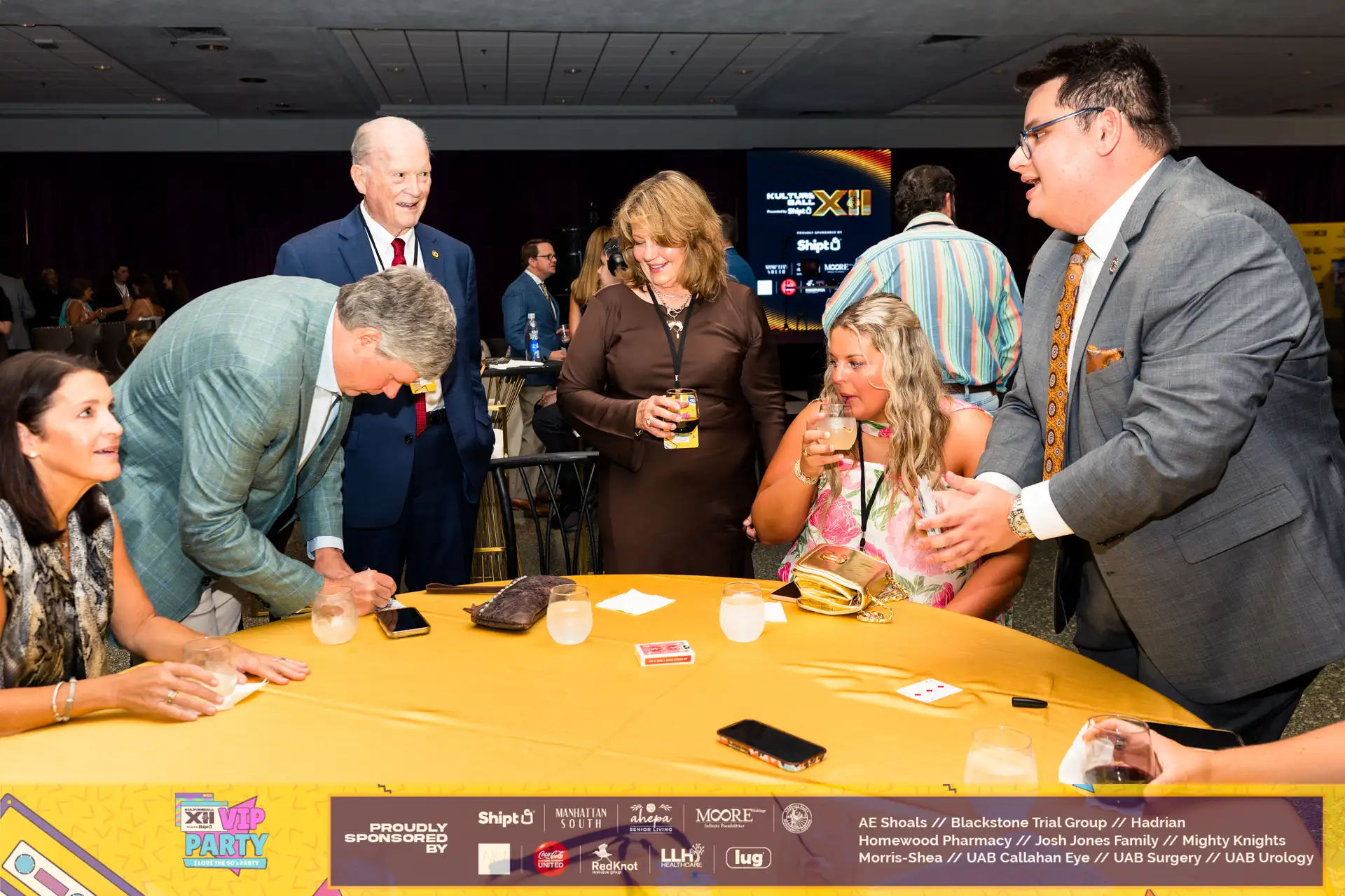 A group of people gathered around a table with drinks and food, enjoying a social event.