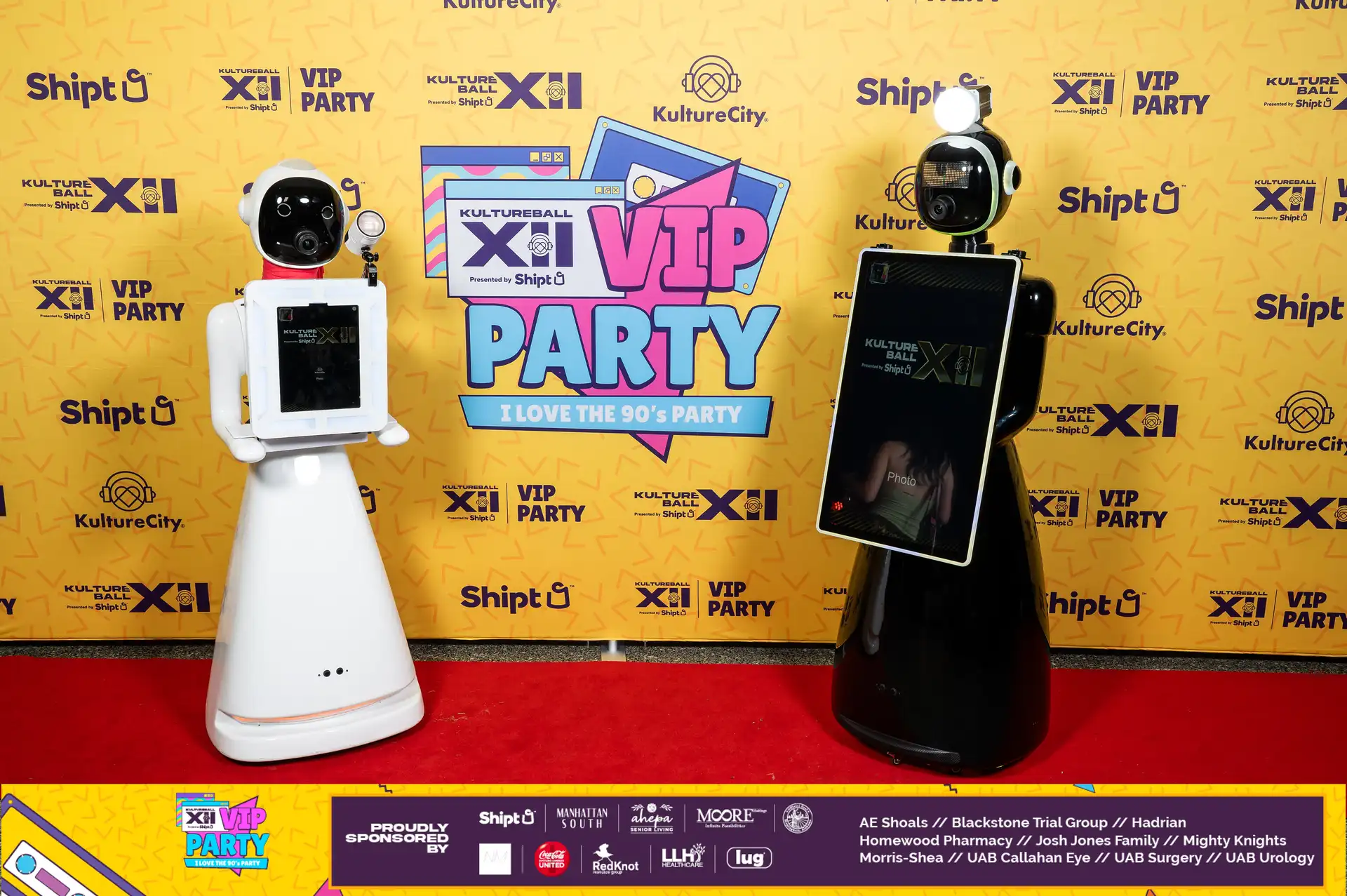 Two robots with cameras on their heads stand in front of a sign for a VIP party.