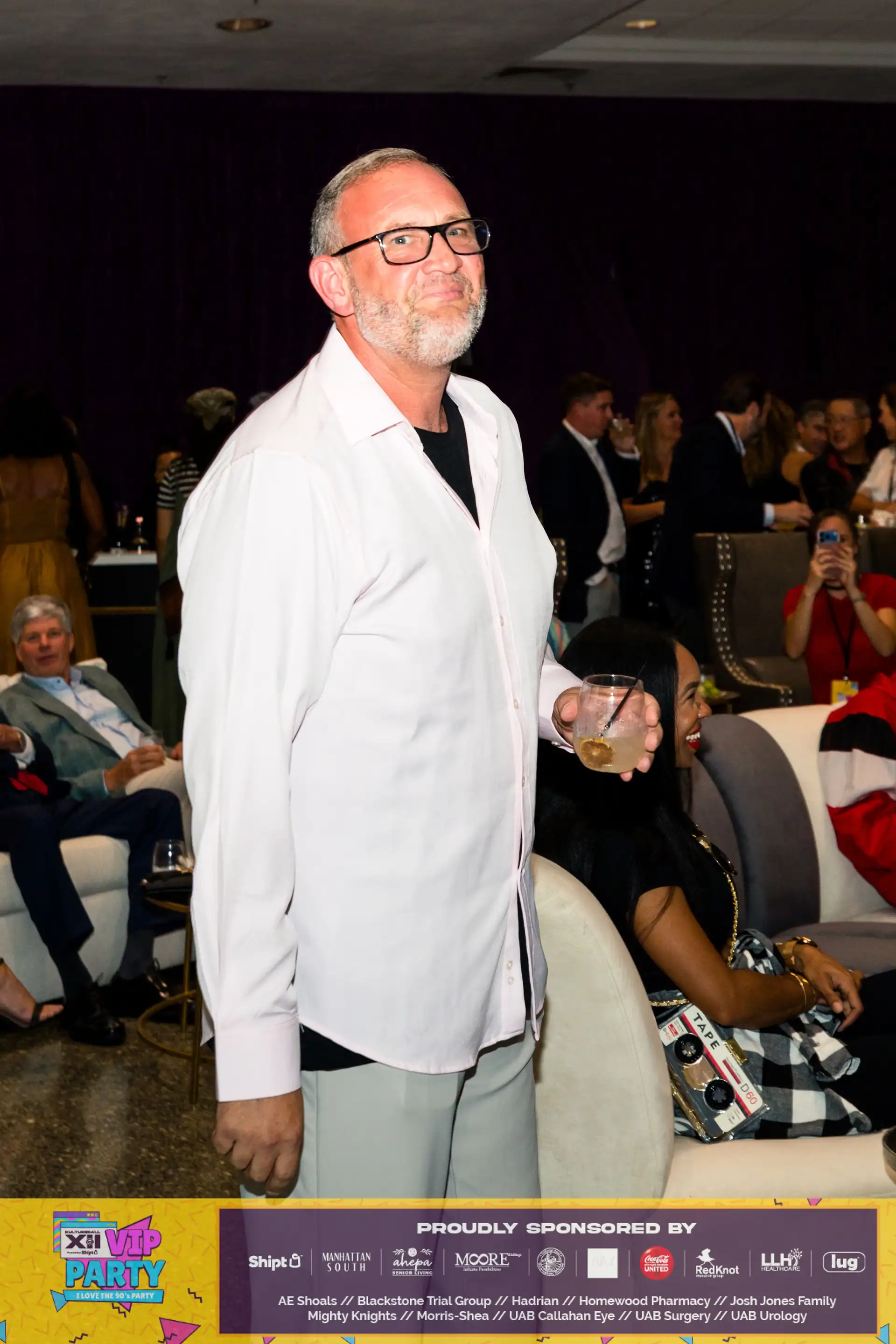 A man in a white shirt holding a glass of lemonade at a social event.