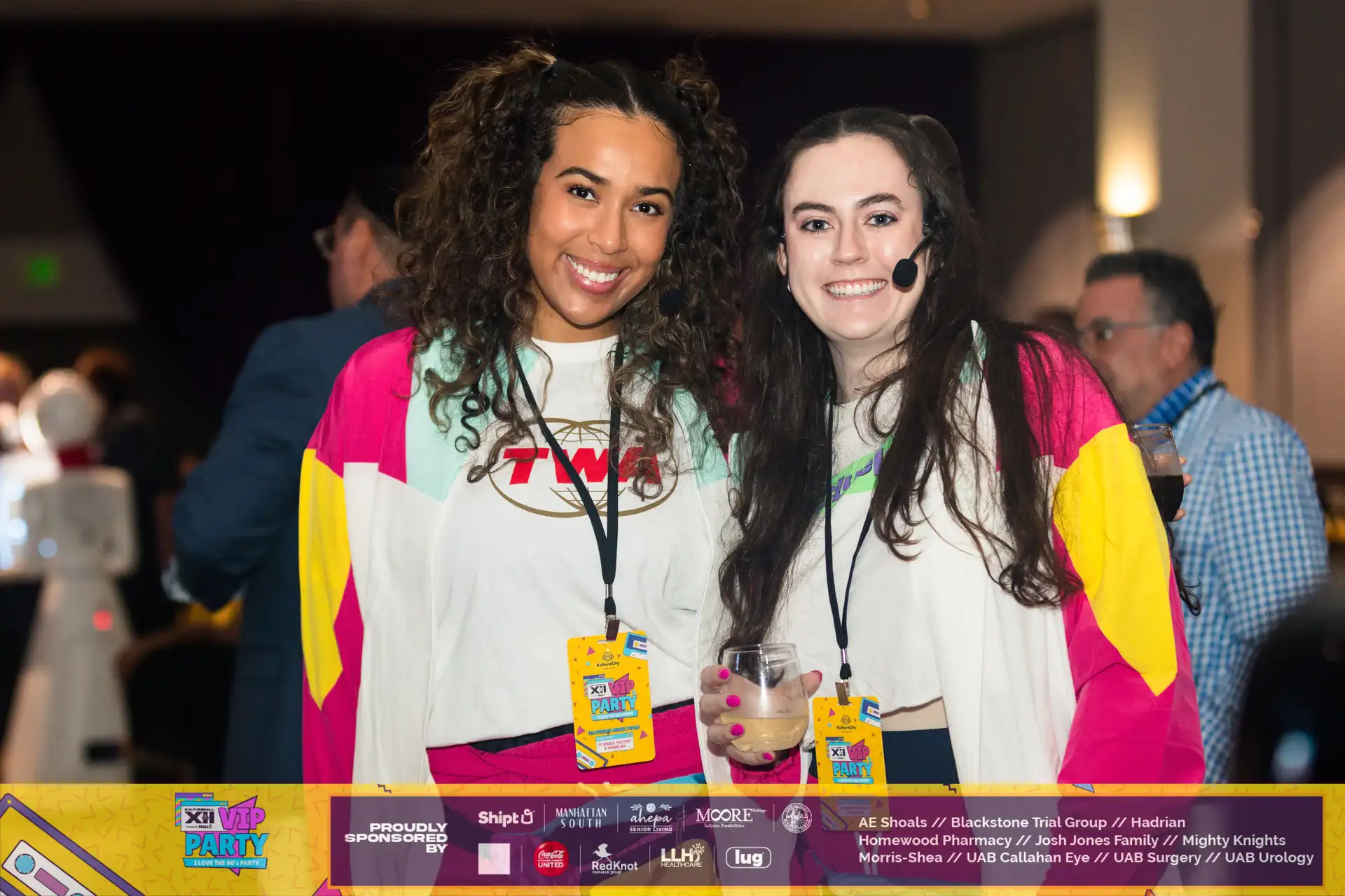Two women in colorful shirts are smiling and holding glasses of Touch O Magic Lemonade.